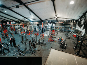 Wide-angle view of a fully equipped gym floor featuring strength machines, free weights, and functional training equipment in a spacious, industrial-style fitness facility.